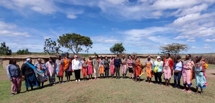 A panoramic shot of African women and Fordham students and staff standing side by side against a bright blue sky