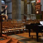 One man stands and sings; another sits and plays at a piano.